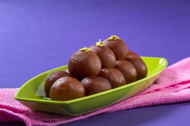 Hint Tatlısı Gulab Jamun 'u tabakta mor arka planda peçeteyle