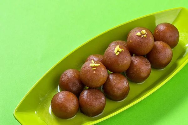 Gulab jamun im Teller auf grünem Hintergrund. indisches Dessert oder süßes Gericht. — Stockfoto