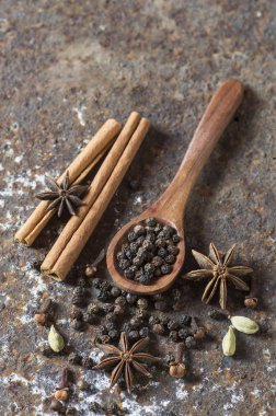 Baharatlar ve bitkiler. Yiyecek ve mutfak malzemeleri. Tarçın çubukları, anason yıldızları, karabiber ve dokulu arka planda kakule..