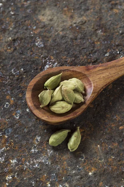 Cardamom pods in wooden spoon on a textured background — Stock Photo, Image