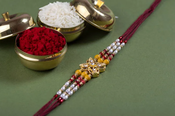 Indian festival: Raksha Bandhan background with an elegant Rakhi, Rice Grains and Kumkum. A traditional Indian wrist band which is a symbol of love between Brothers and Sisters. — Stock Photo, Image