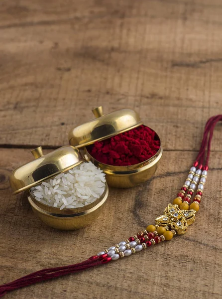 A Rakhi with rice grains and kumkum on wooden background. An Indian festive background. — Stock Photo, Image