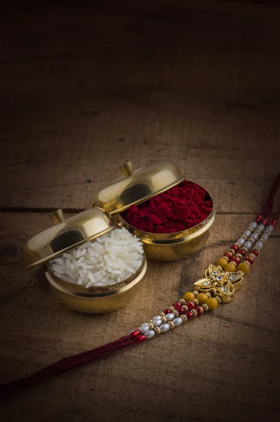 A Rakhi with rice grains and kumkum on wooden background. An Indian festive background. — Stock Photo, Image