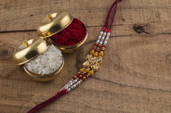 A Rakhi with rice grains and kumkum on wooden background. An Indian festive background.