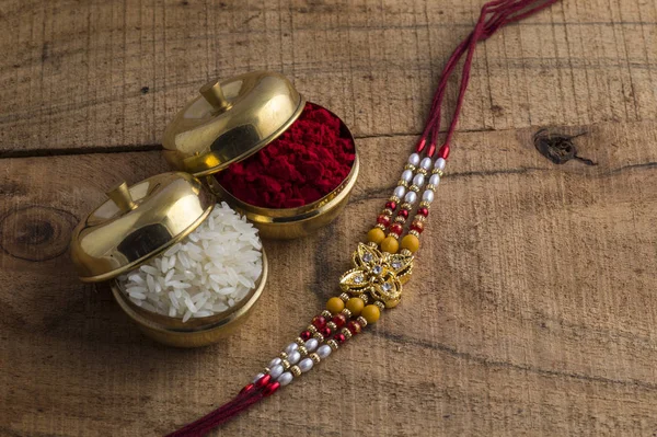 Ракхі з рисовими зернами і кумкумом на дерев'яному тлі. Індійське святкове тло. — стокове фото
