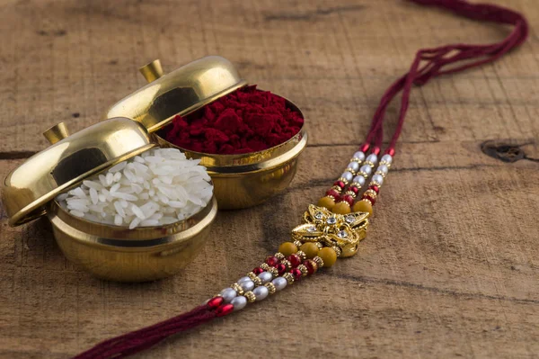 A Rakhi with rice grains and kumkum on wooden background. An Indian festive background.