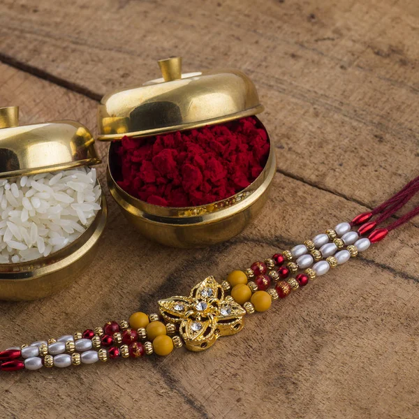 A Rakhi with rice grains and kumkum on wooden background. An Indian festive background.