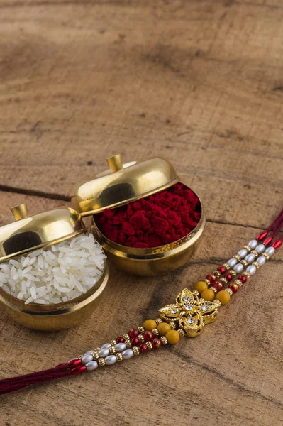 Un Rakhi cu boabe de orez și kumkum pe fundal din lemn. Un fundal festiv indian . — Fotografie, imagine de stoc