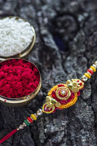 A Rakhi with rice grains and kumkum on wooden background. An Indian festive background.