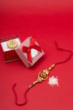 Raakhi ve Raksha Bandhan vesilesiyle ablasına bir hediye. Hint festivali Raksha Bandhan kırmızı arka planda zarif bir Rakhi ile arka planda.