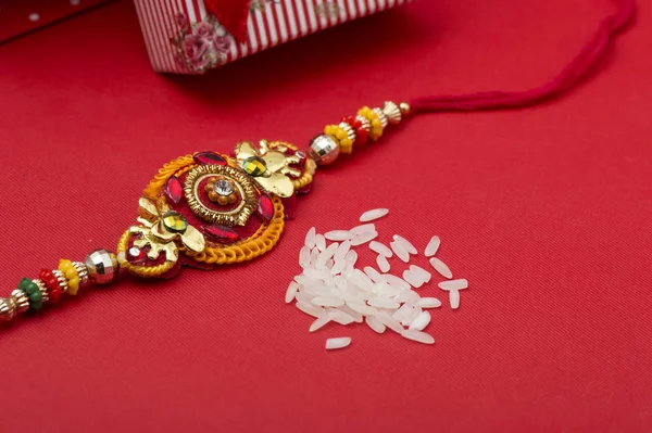 Raakhi and a gift for the sister given by brother on the occasion of Raksha Bandhan. Indian festival Raksha Bandhan background with an elegant Rakhi on red background. — Stock Photo, Image