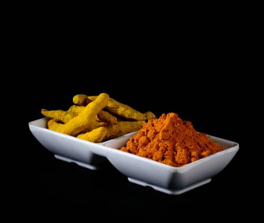 Beyaz tabakta kuru zerdeçal tozu ve kökleri veya kabukları