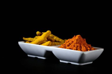 Beyaz tabakta kuru zerdeçal tozu ve kökleri veya kabukları