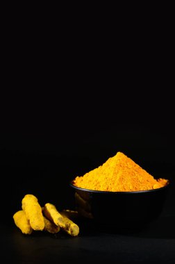 Zerdeçal tozu ve kökleri ya da siyah arka plandaki siyah kasede kabukları.