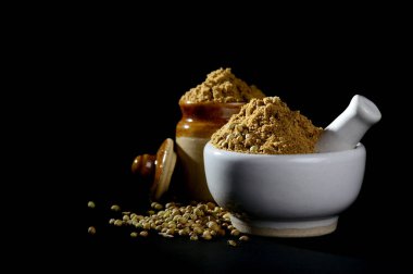 Kişniş tozu ve siyah arka planda tohumlarla harç ve tokmak.