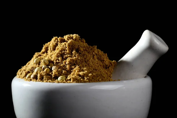 Coriander Powder and seeds with mortar and pestle on black background.