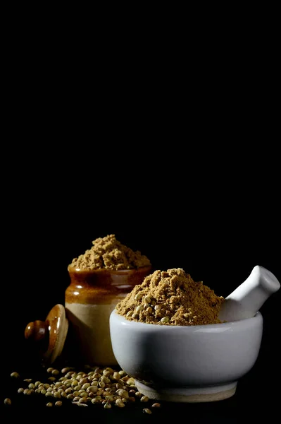 mortar and pestle with Coriander Powder and seeds on black background.