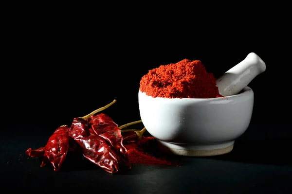 Red Chili Pepper powder in pestle with mortar and Red Chili Peppers on black background