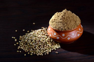 Kişniş tohumu ve toz kişniş, ahşap arka planda kil kapta..