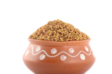 Beyaz arka planda izole edilmiş kil çömlekte FenuGreek tohumları