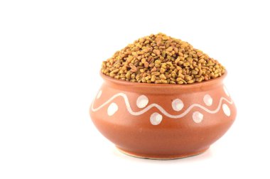 Beyaz arka planda izole edilmiş kil çömlekte FenuGreek tohumları