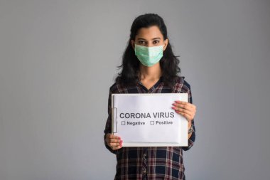 Tıbbi maskeli genç bir kadın Coronavirus salgını panosunu tutuyor, Covid-19.