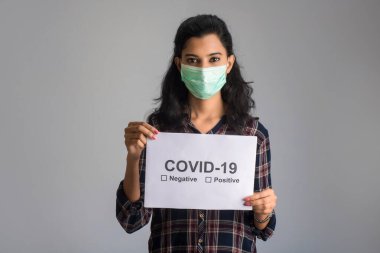 Tıbbi maskeli genç bir kadın Coronavirus salgını panosunu tutuyor, Covid-19.