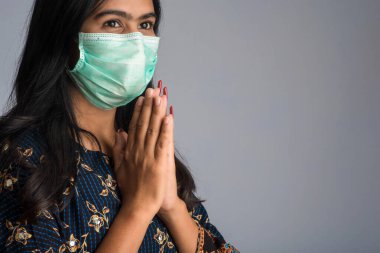 Tıbbi maske takan bir kızın portresi Namaste jesti ile selamlaşıyor..