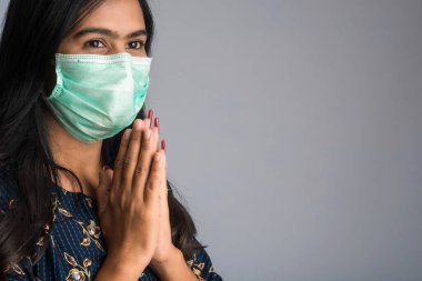 Tıbbi maske takan bir kızın portresi Namaste jesti ile selamlaşıyor..