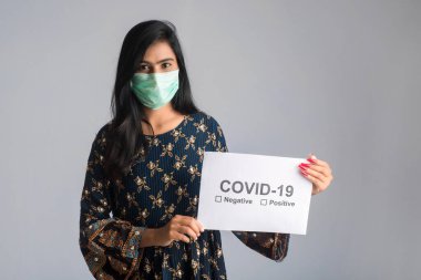 Tıbbi maskeli genç bir kadın Coronavirus salgını panosunu tutuyor, Covid-19.