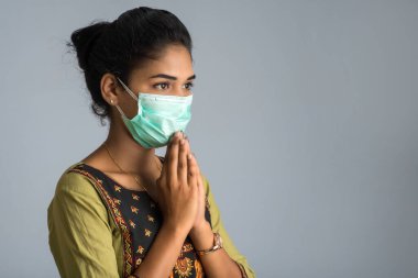 Tıbbi maske takan bir kızın portresi Namaste jesti ile selamlaşıyor..