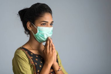 Tıbbi maske takan bir kızın portresi Namaste jesti ile selamlaşıyor..