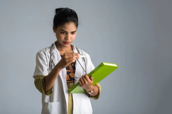 Beautiful young woman doctor with thermometer and report or book