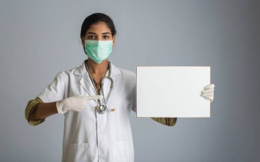 Tıbbi maskeli genç bir kadın doktor elinde boş bir tahta, Coronavirus salgını konsepti, Covid-19.