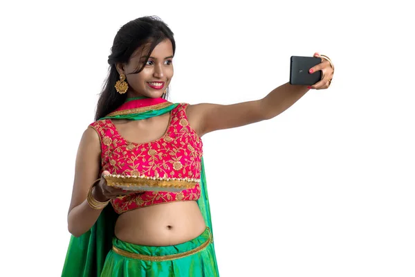 美しい若いです幸せな女の子は白い背景にスマートフォンを使用して光Diwaliの祭りの間に粘土ランプやDiyaで自撮り — ストック写真