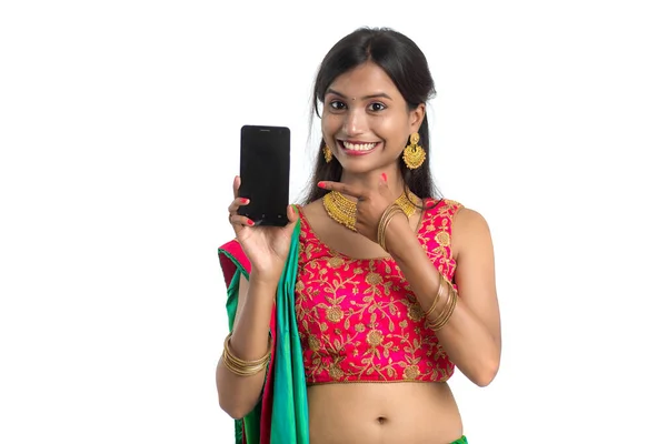 若いインドの伝統的な女の子は 携帯電話やスマートフォンを使用して 白い背景に空白の画面のスマートフォンを示しています — ストック写真