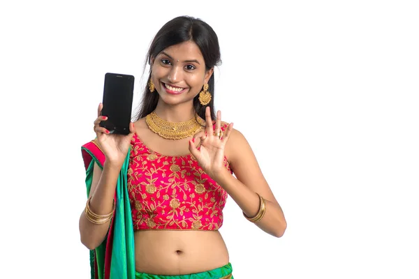 若いインドの伝統的な女の子は 携帯電話やスマートフォンを使用して 白い背景に空白の画面のスマートフォンを示しています — ストック写真