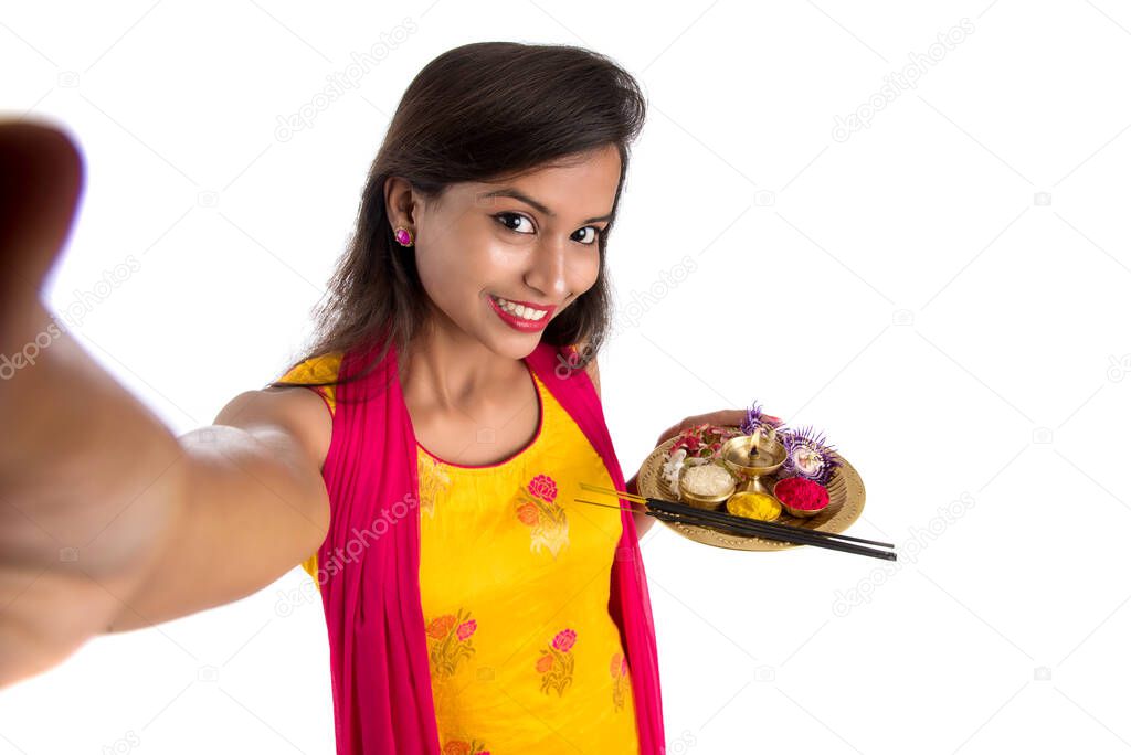 Beautiful young happy girl taking selfie with pooja thali using a mobile phone or smartphone on a white background