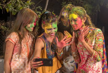 Holi Festivali 'nde akıllı telefon kullanarak eğlenen ve selfie çeken bir grup genç kız. Festival ve teknoloji konsepti