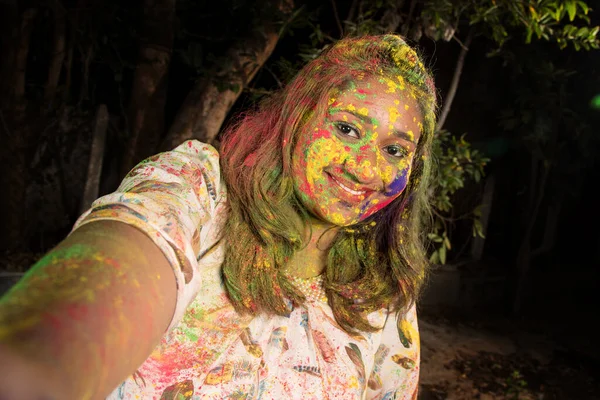 在Holi音乐节上 一个面容五彩斑斓的小女孩用智能手机或相机自拍 节庆与科技概念 — 图库照片