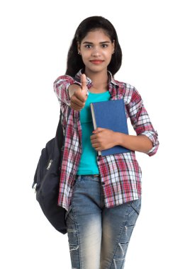 Sırt çantalı genç Hintli kadın ayakta duruyor ve elinde defterlerle beyaz bir arka planda poz veriyor..