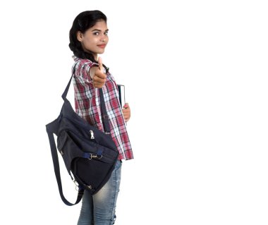 Sırt çantalı genç Hintli kadın ayakta duruyor ve elinde defterlerle beyaz bir arka planda poz veriyor..