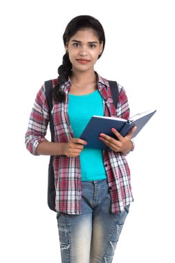 Sırt çantalı genç Hintli kadın ayakta duruyor ve elinde defterlerle beyaz bir arka planda poz veriyor..