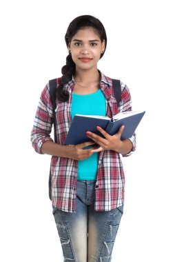 Sırt çantalı genç Hintli kadın ayakta duruyor ve elinde defterlerle beyaz bir arka planda poz veriyor..