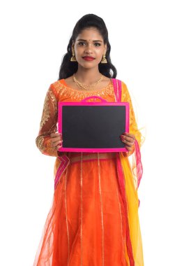 Elinde beyaz bir arka planda boş bir tahtayla poz veren güzel bir genç kadın.