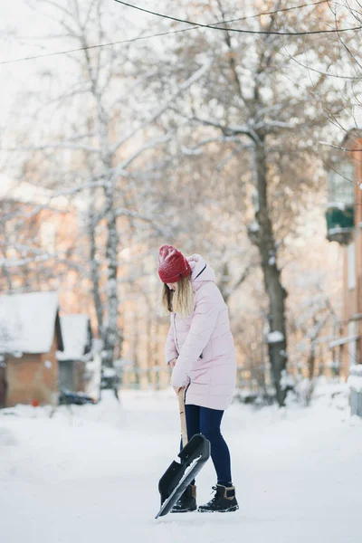 Joven adolescente limpia la nieve cerca de la casa, sosteniendo una pala y remo pasar tiempo —  Fotos de Stock