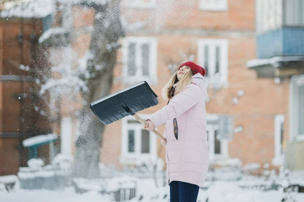 Young teen girl cleans snow near the house, holding a shovel and paddle spend time