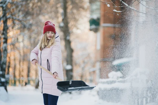 Junges Teenie-Mädchen räumt Schnee in der Nähe des Hauses, hält Schaufel und Paddel in der Hand — Stockfoto