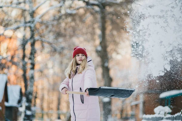 Junges Teenie-Mädchen räumt Schnee in der Nähe des Hauses, hält Schaufel und Paddel in der Hand — Stockfoto