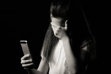 Bir cep telefonu ile koyu arka planda yatak odasında yatağın üzerinde oturan ağıt tutmak tek üzücü teen